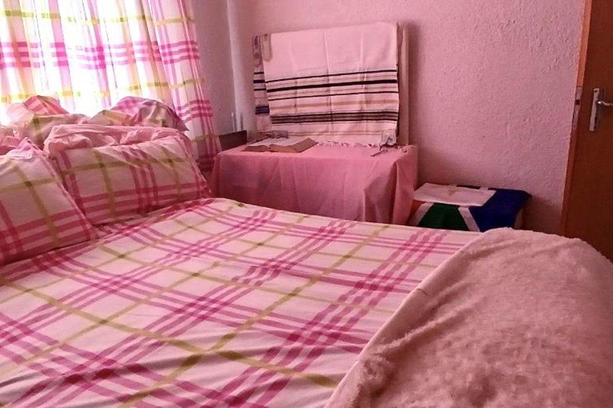A bedroom featuring tiled flooring and a standard wooden door, providing a functional space for rest.