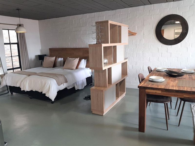An open-plan studio apartment featuring exposed brick walls, a painted timber ceiling, and smooth epoxy flooring with industrial-style window detailing.