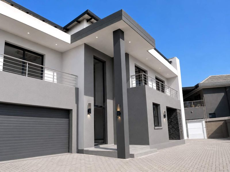 Modern double-story residence featuring a sleek grey and white facade, double garage, and upper-level balconies with stainless steel railings.