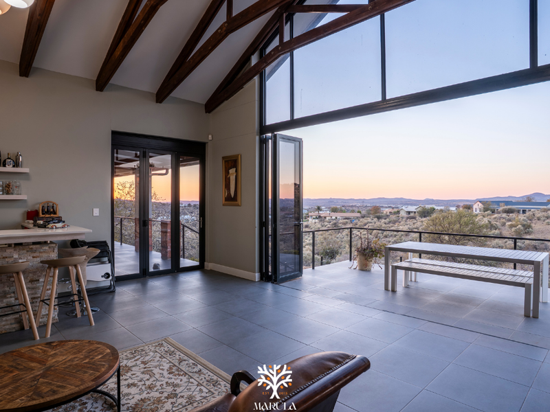 Spacious open-plan living area featuring exposed timber trusses, large bi-fold doors opening to a patio, and panoramic views.