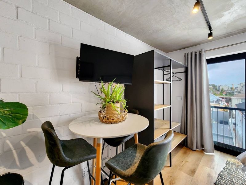 Modern bedroom featuring an exposed concrete ceiling, painted brick wall, and direct access to a private balcony through a sliding glass door.