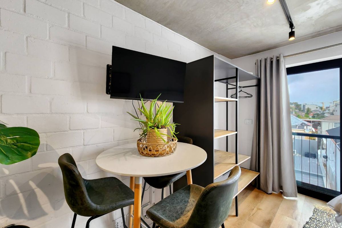 Modern bedroom featuring an exposed concrete ceiling, painted brick wall, and direct access to a private balcony through a sliding glass door.