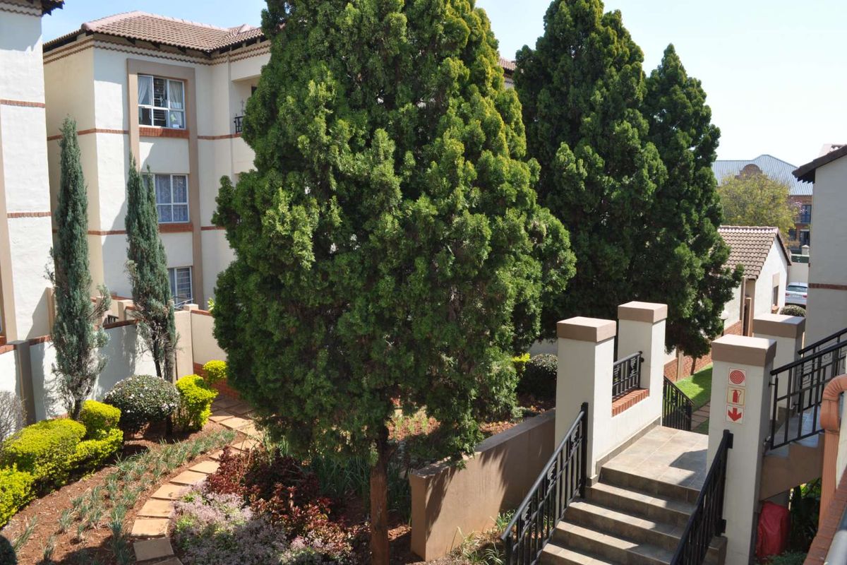 A well-maintained exterior view of the apartment complex featuring a landscaped garden, tiled staircase with wrought iron railings, and paved pathways.