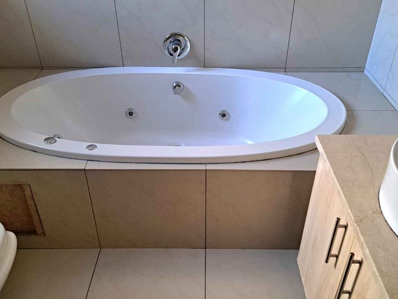 A bathroom featuring a built-in jetted bathtub with tiled surround, a vanity cabinet with a vessel sink, and ceramic tiling throughout.