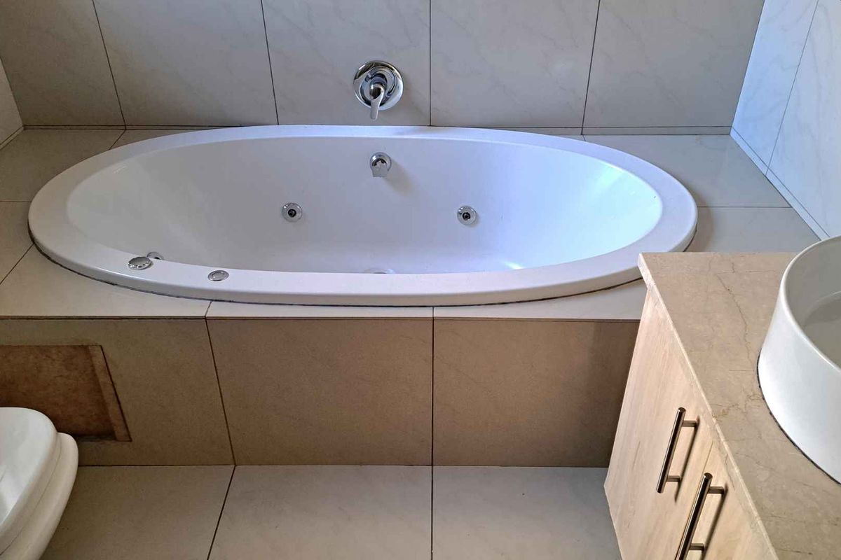 A bathroom featuring a built-in jetted bathtub with tiled surround, a vanity cabinet with a vessel sink, and ceramic tiling throughout.