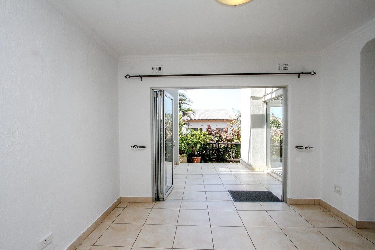 An empty, bright living area featuring tiled flooring and large bi-fold glass doors that open onto a patio space.