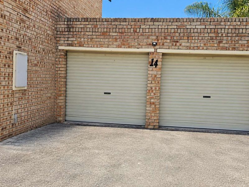 Exterior view of a double garage featuring face brick construction and roller doors, situated with an asphalt driveway approach.