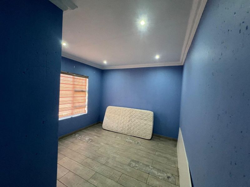 An empty bedroom featuring blue painted walls, tiled flooring, recessed downlights, and crown molding, requiring minor cosmetic updates.