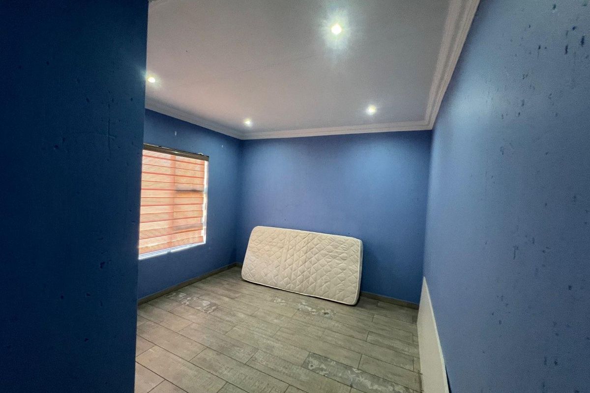 An empty bedroom featuring blue painted walls, tiled flooring, recessed downlights, and crown molding, requiring minor cosmetic updates.