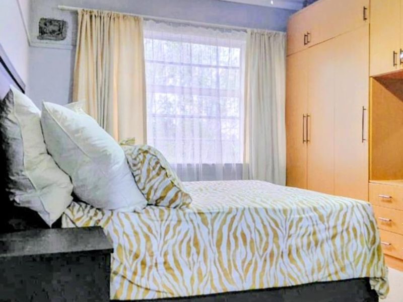 A bedroom featuring built-in wooden cupboards, a ceiling fan, and natural light through a window with curtain rails.