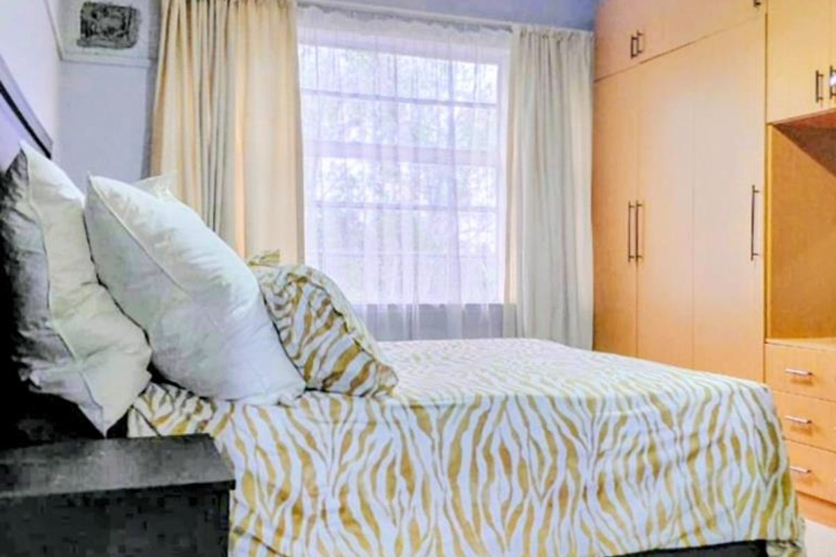 A bedroom featuring built-in wooden cupboards, a ceiling fan, and natural light through a window with curtain rails.