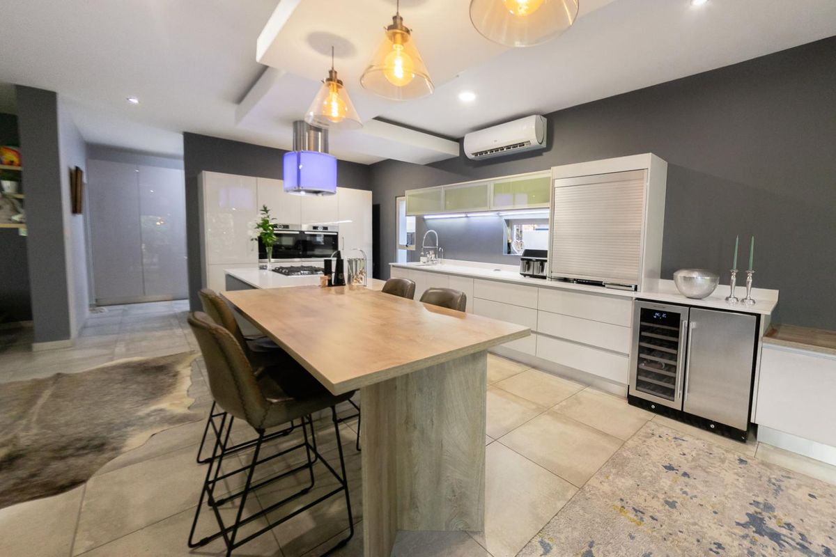Modern open-plan kitchen featuring high-gloss cabinetry, integrated appliances, a built-in wine cooler, and a central breakfast island with pendant lighting.