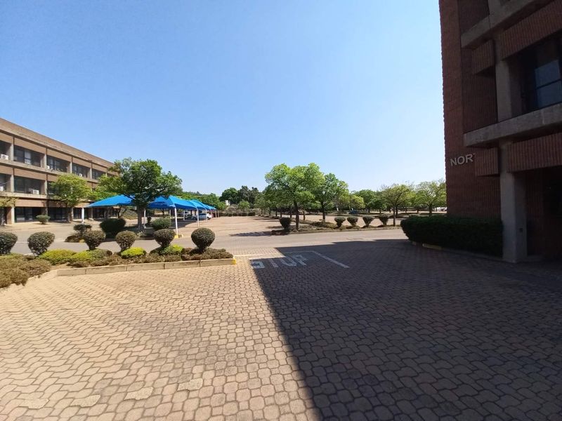 Exterior view of the office park grounds featuring paved parking areas, landscaped garden beds, and covered parking bays.