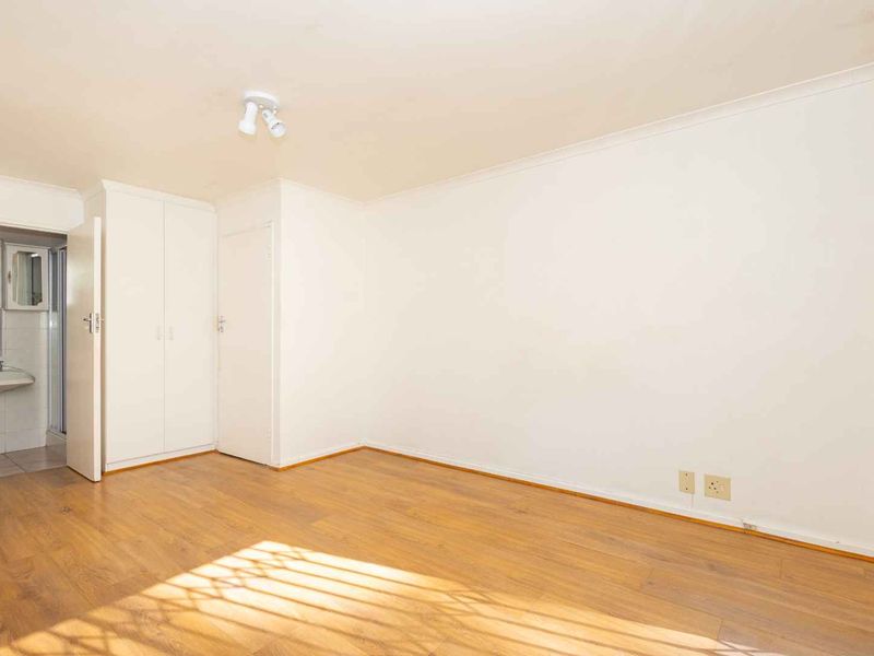 A bright, empty bedroom featuring laminate flooring, built-in cupboards, and direct access to an en-suite bathroom.