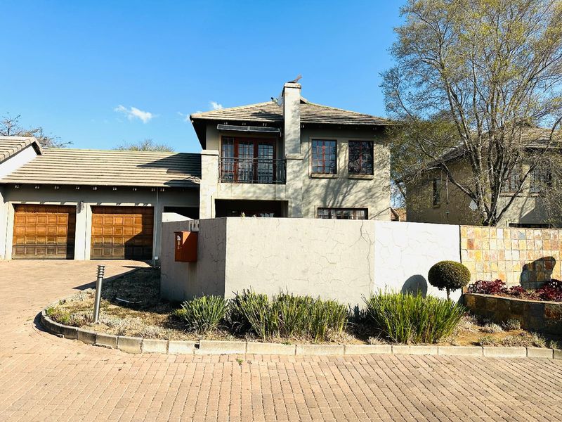 Front exterior view of a double-story townhouse featuring a double garage, paved driveway, and a balcony with a chimney.