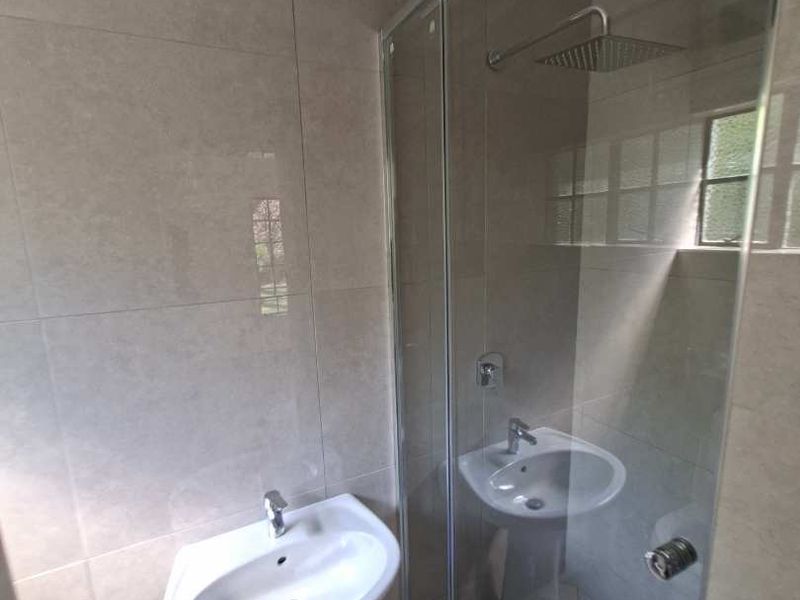 Modern bathroom featuring a pedestal basin and a glass-enclosed shower with a rain shower head and neutral wall tiling.