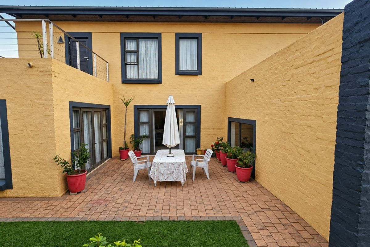A well-maintained rear courtyard featuring a paved patio area, direct access to the home via sliding doors, and an upper-level balcony with metal railings.
