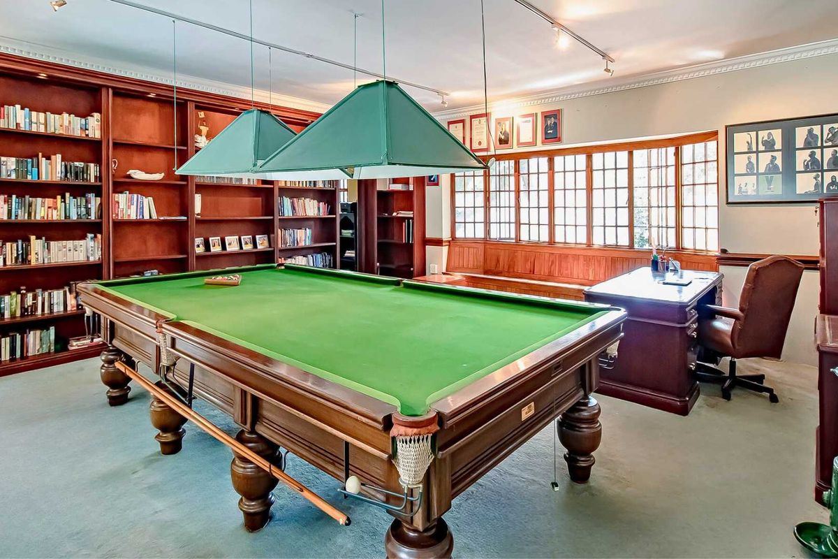 Spacious games room featuring extensive built-in wooden cabinetry, large bay windows with timber frames, and dedicated overhead lighting for the billiards area.
