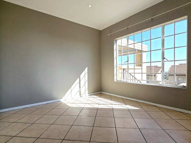 A bright, empty bedroom featuring neutral tiled flooring, built-in cupboards, and a large grid-pattern window allowing for ample natural light.