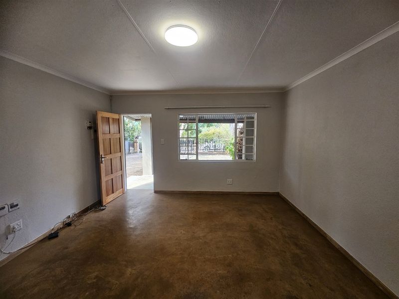 A bright, empty living room featuring polished concrete floors, a timber door, and a window with security bars, offering a clean, neutral canvas.