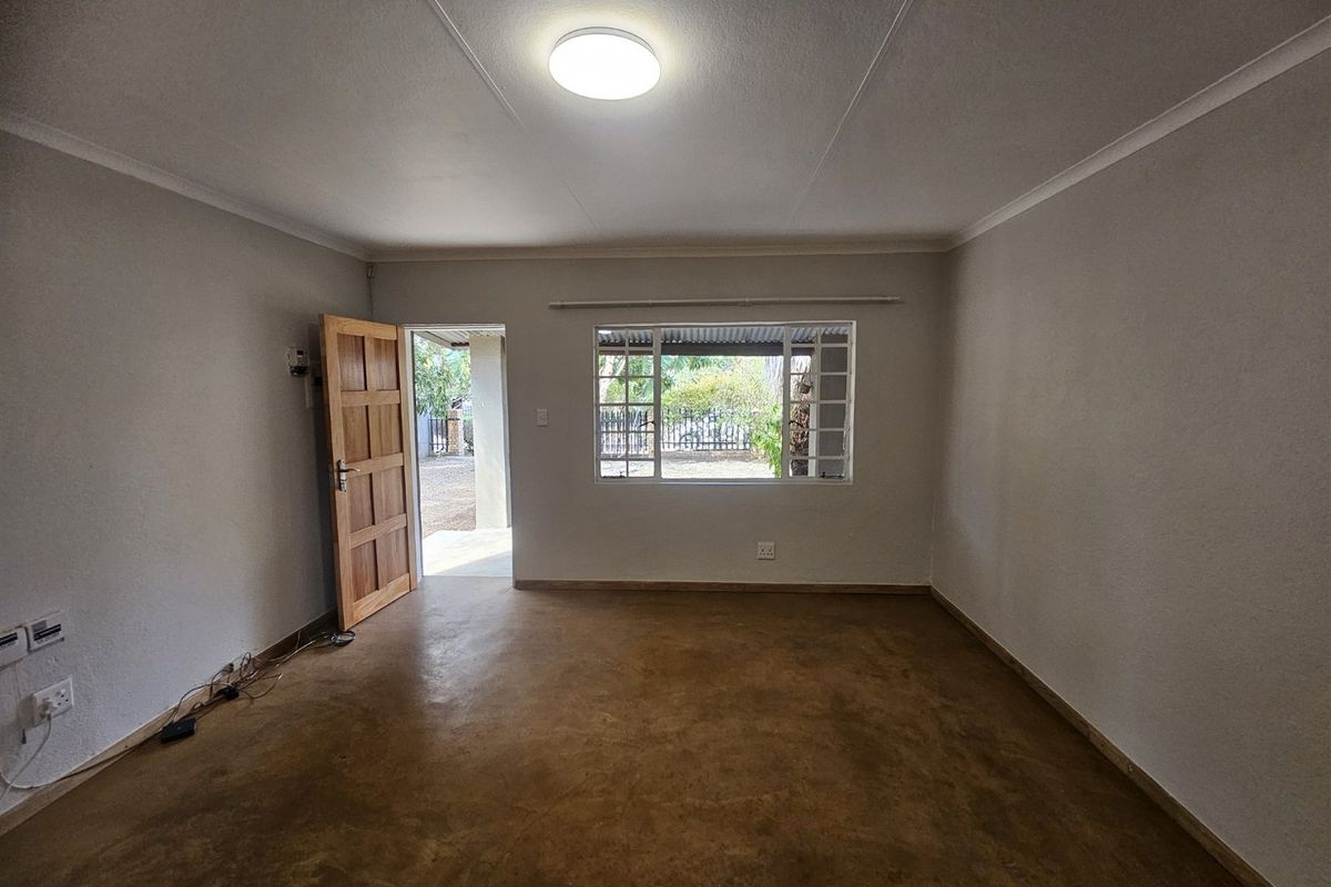 A bright, empty living room featuring polished concrete floors, a timber door, and a window with security bars, offering a clean, neutral canvas.