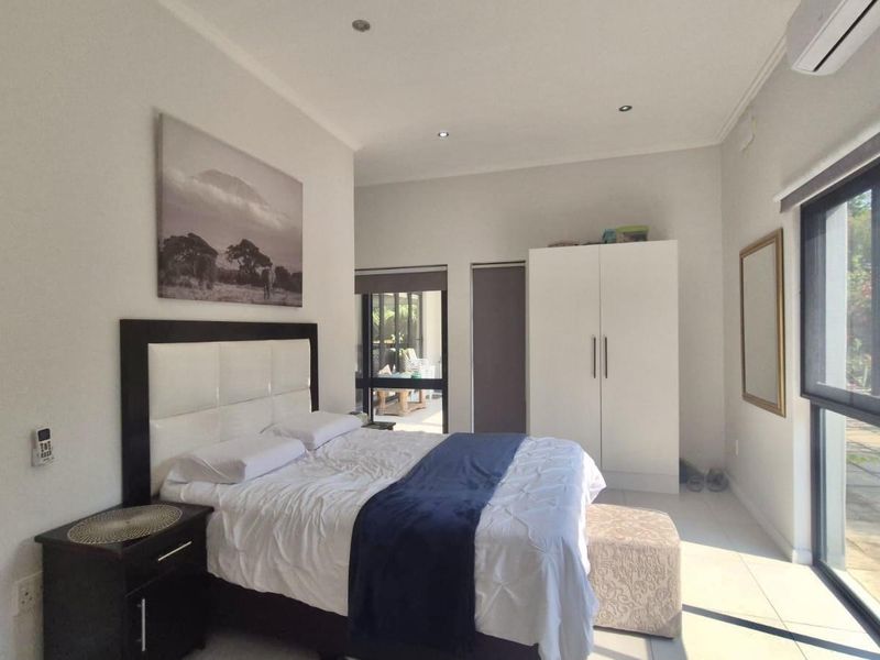 A bright bedroom featuring tiled flooring, recessed downlights, a split-system air conditioner, and large sliding glass doors providing access to the outdoor area.