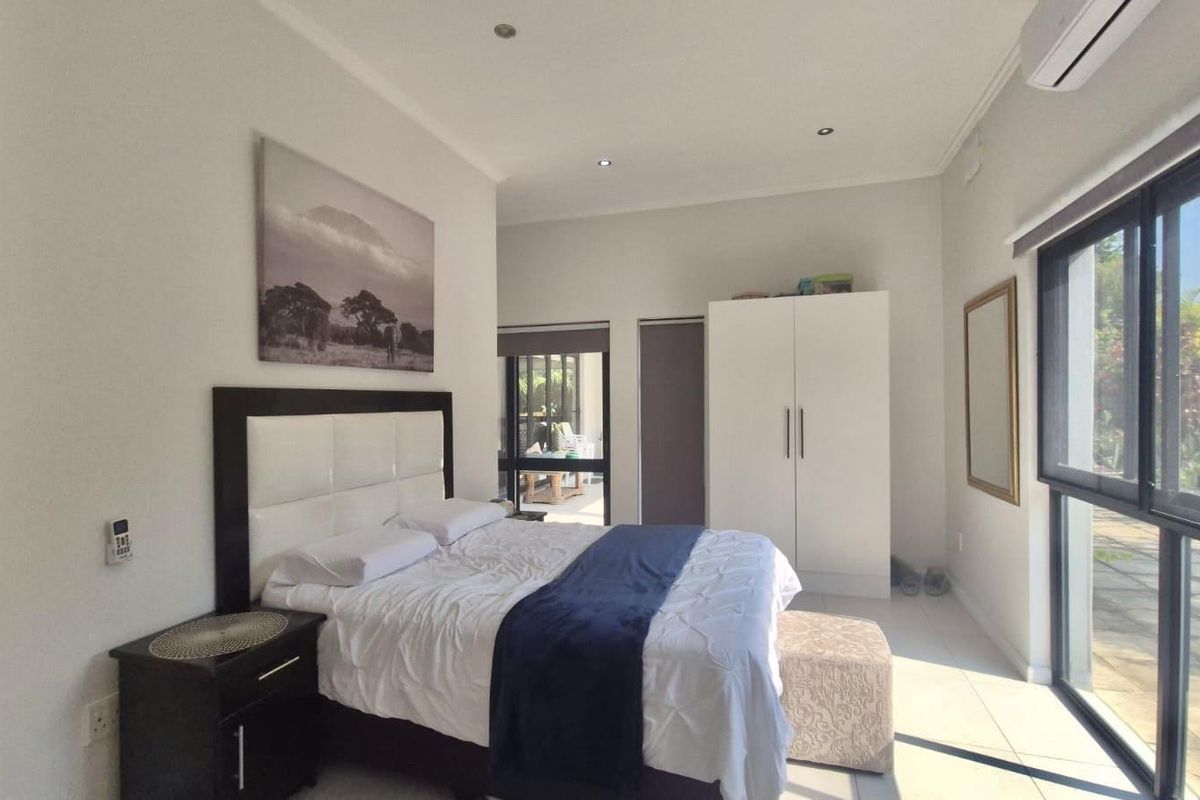 A bright bedroom featuring tiled flooring, recessed downlights, a split-system air conditioner, and large sliding glass doors providing access to the outdoor area.