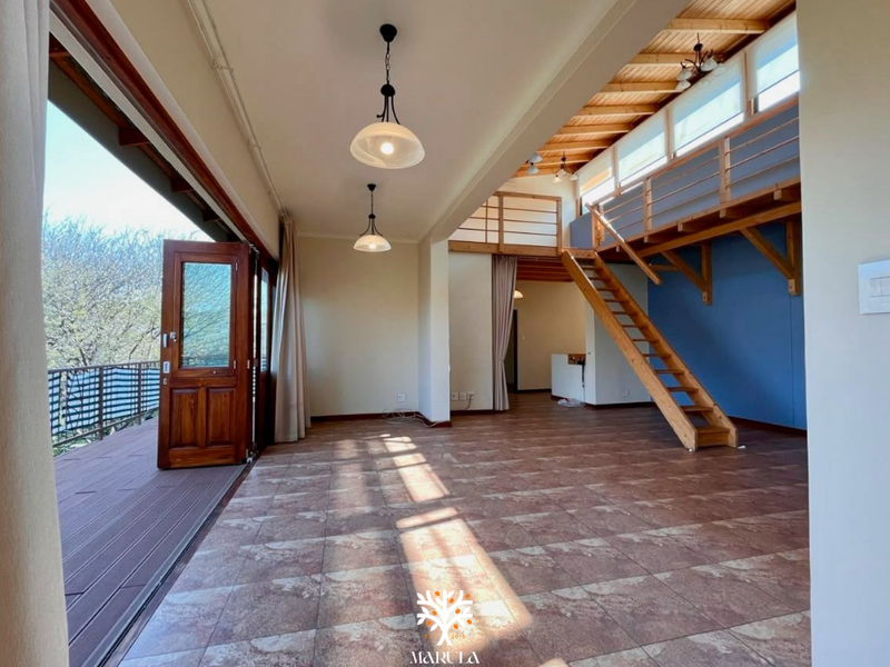 Spacious open-plan living area featuring a timber staircase leading to a mezzanine level, tiled flooring, and direct access to an outdoor balcony.