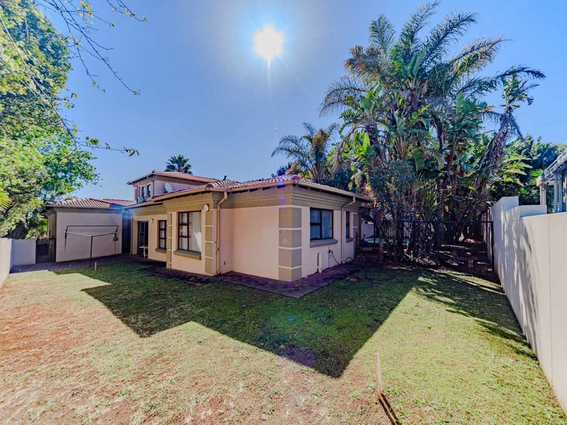 Rear view of the property featuring a paved patio area, established garden with mature trees, and perimeter boundary walls.