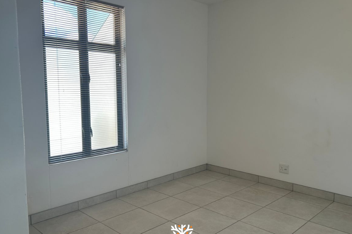 A bright, empty bedroom featuring neutral floor tiles, white walls, and a window fitted with horizontal blinds.