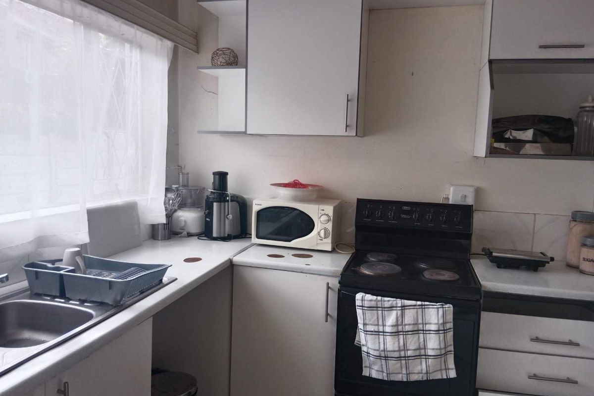 A functional kitchen featuring white cabinetry, laminate countertops, a stainless steel sink, and a freestanding electric stove with tiled splashback.