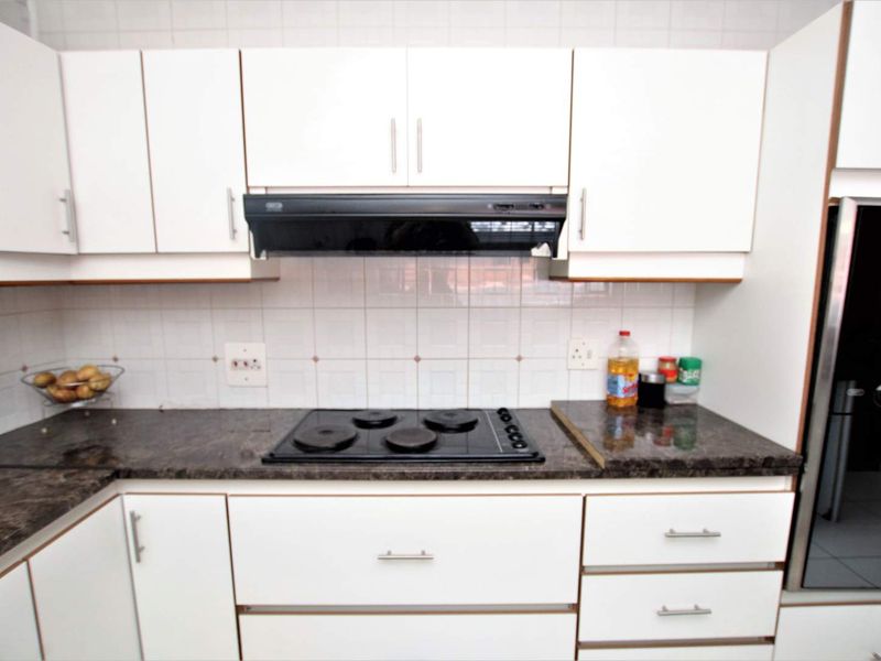 A functional kitchen featuring white cabinetry, dark granite countertops, a built-in electric hob, and an extractor fan with a tiled backsplash.