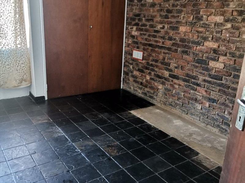 An empty bedroom featuring a rustic exposed brick wall, built-in wooden cupboards, and dark slate tile flooring.
