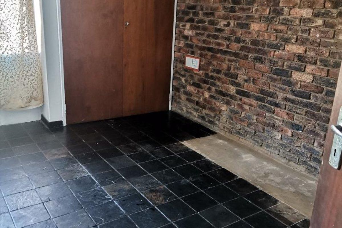 An empty bedroom featuring a rustic exposed brick wall, built-in wooden cupboards, and dark slate tile flooring.