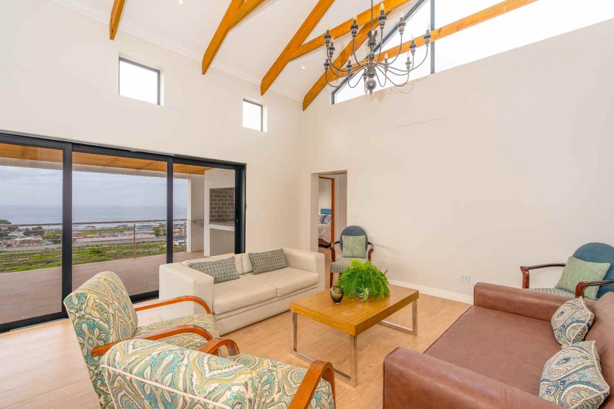 Spacious living area featuring high vaulted ceilings with exposed timber beams, large sliding glass doors, and expansive coastal views.