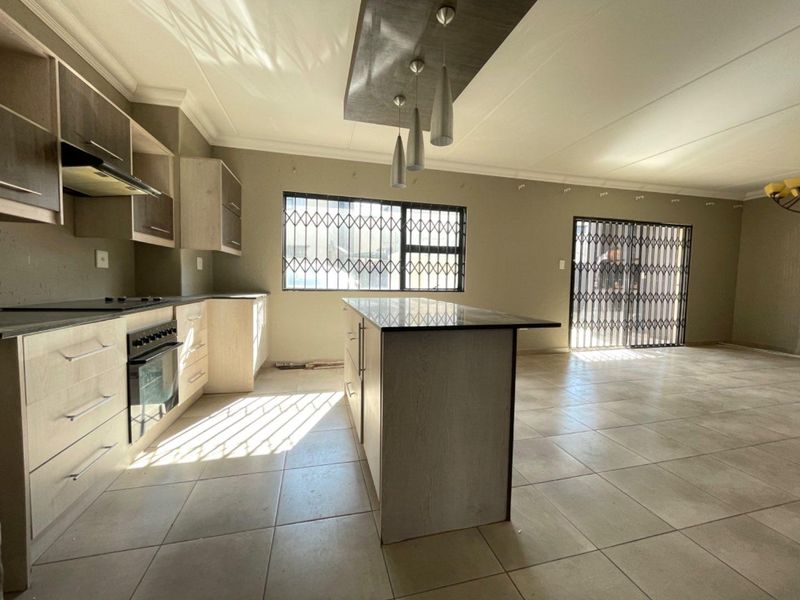 Spacious open-plan kitchen and living area featuring a central island, modern cabinetry, built-in appliances, and tiled flooring with secure access points.