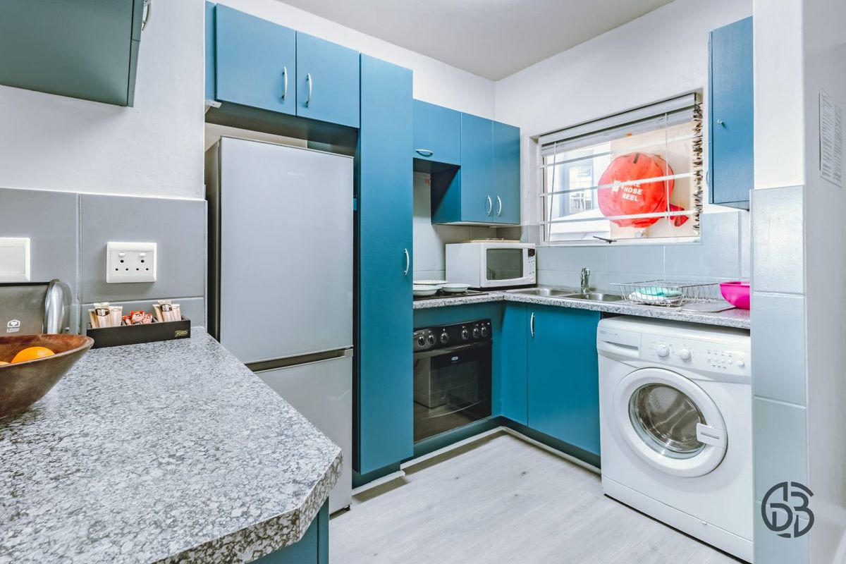 Compact kitchen featuring blue cabinetry, granite-look countertops, integrated oven, and space for a washing machine.