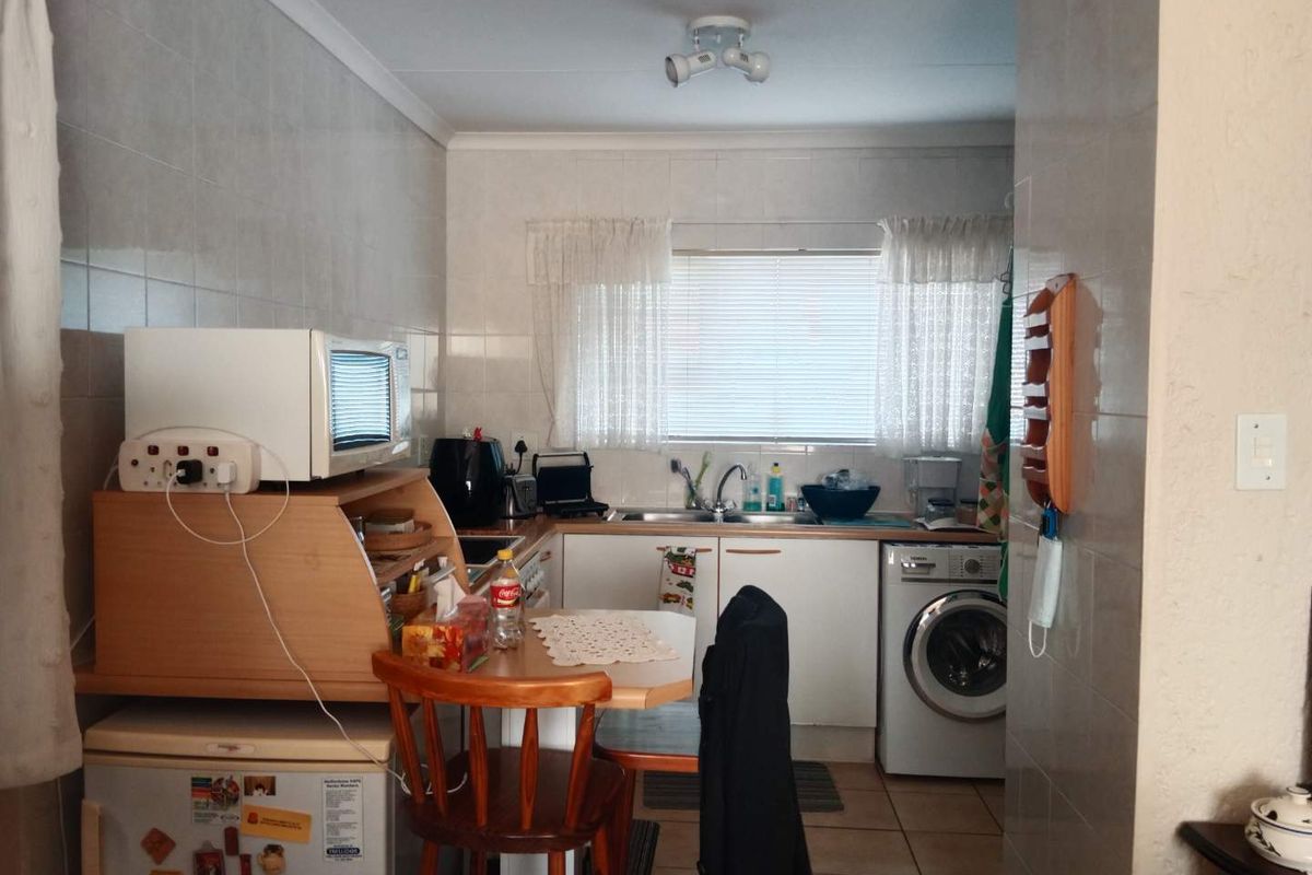 A functional kitchen featuring tiled walls, built-in cabinetry, a stainless steel sink, and space for a washing machine.