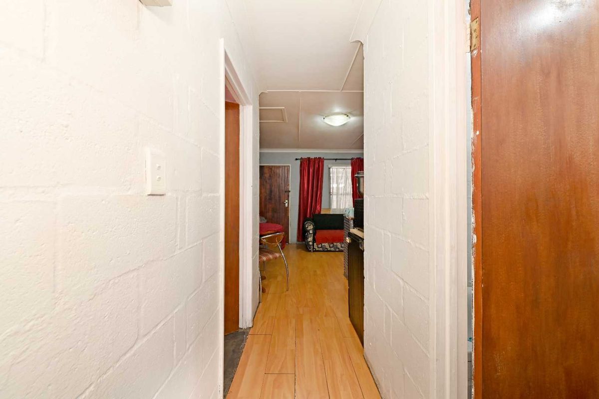 A narrow hallway featuring laminate flooring and painted blockwork walls, providing access to adjacent rooms within the property.