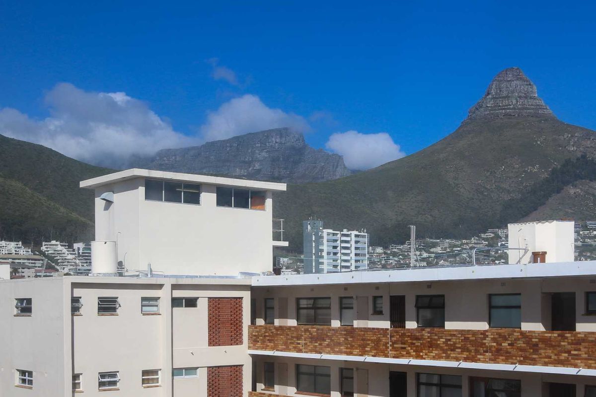 Exterior view of the apartment building facade featuring brick detailing and metal window frames, set against a prominent mountain backdrop.