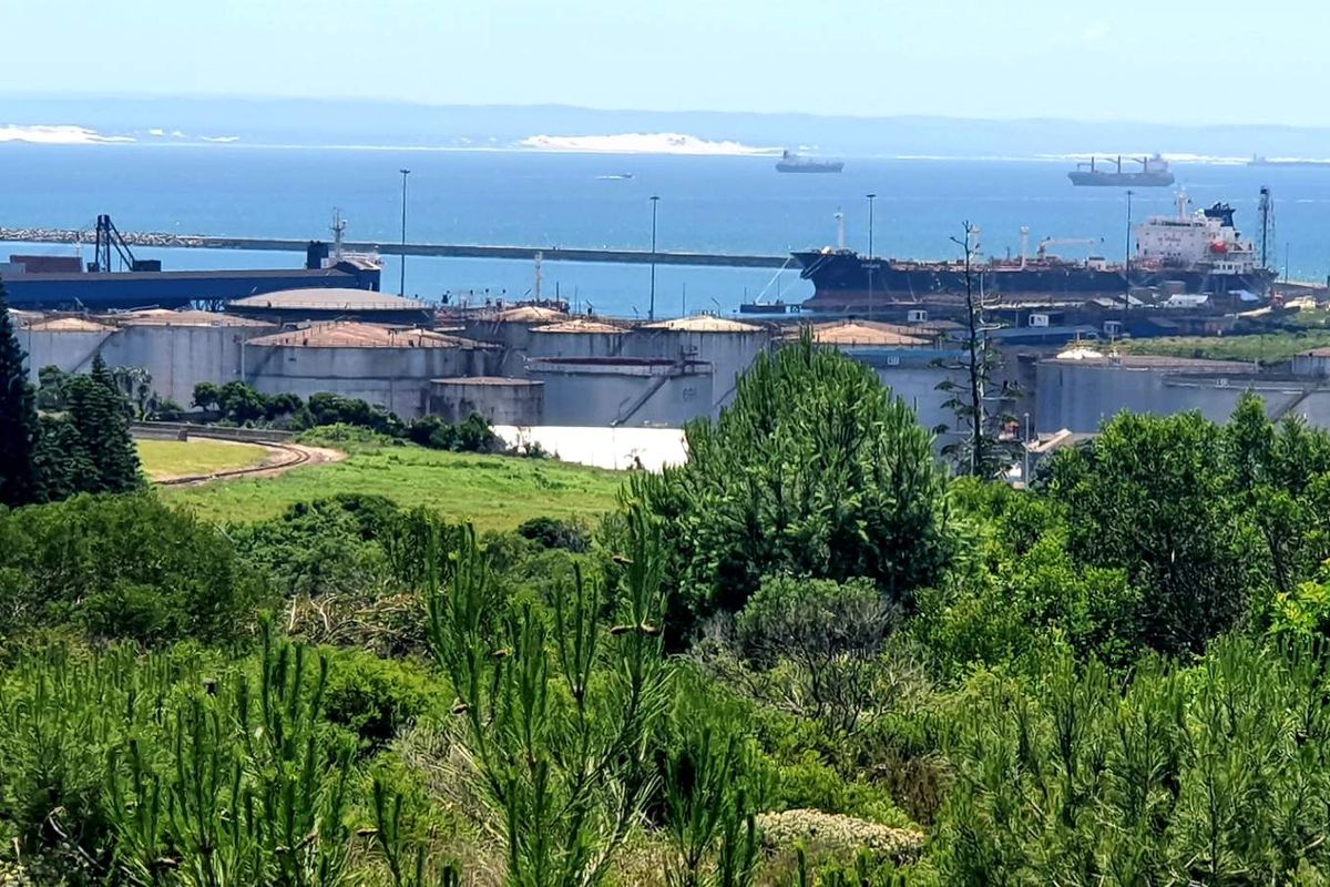 A wide-angle view overlooking a coastal industrial port area with large storage tanks, shipping vessels, and surrounding natural vegetation.