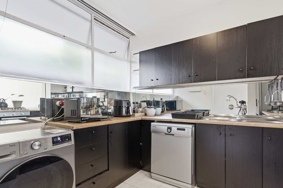 Functional kitchen featuring dark wood cabinetry, wooden countertops, a mirrored backsplash, and integrated appliances including a dishwasher and built-in oven.