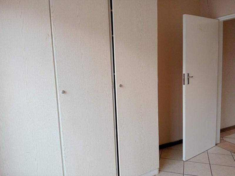 A bedroom interior featuring built-in cupboards and tiled flooring, showing signs of minor wear on the wall finish.