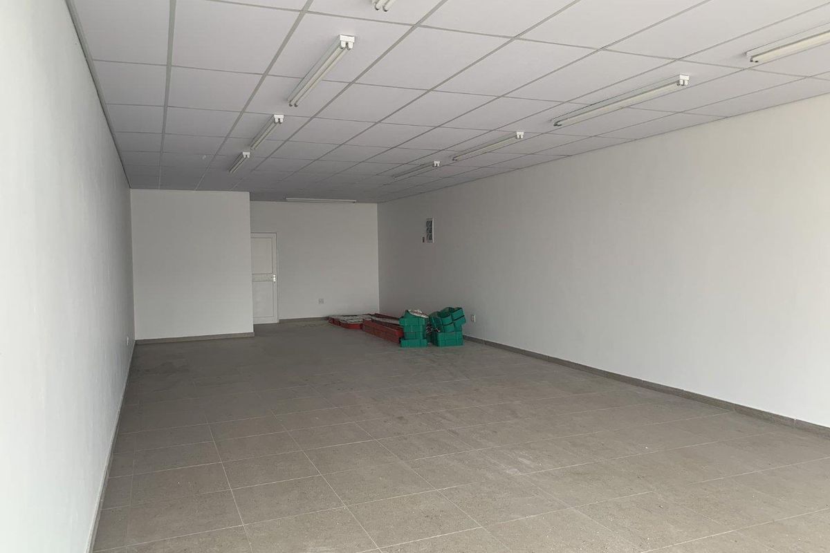 A vacant open-plan retail space featuring neutral tiled flooring, a suspended ceiling with integrated lighting, and clean white walls.