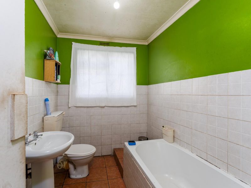 A dated bathroom featuring a pedestal basin, toilet, and bathtub with tiled finishes, requiring cosmetic updates to improve its overall condition.