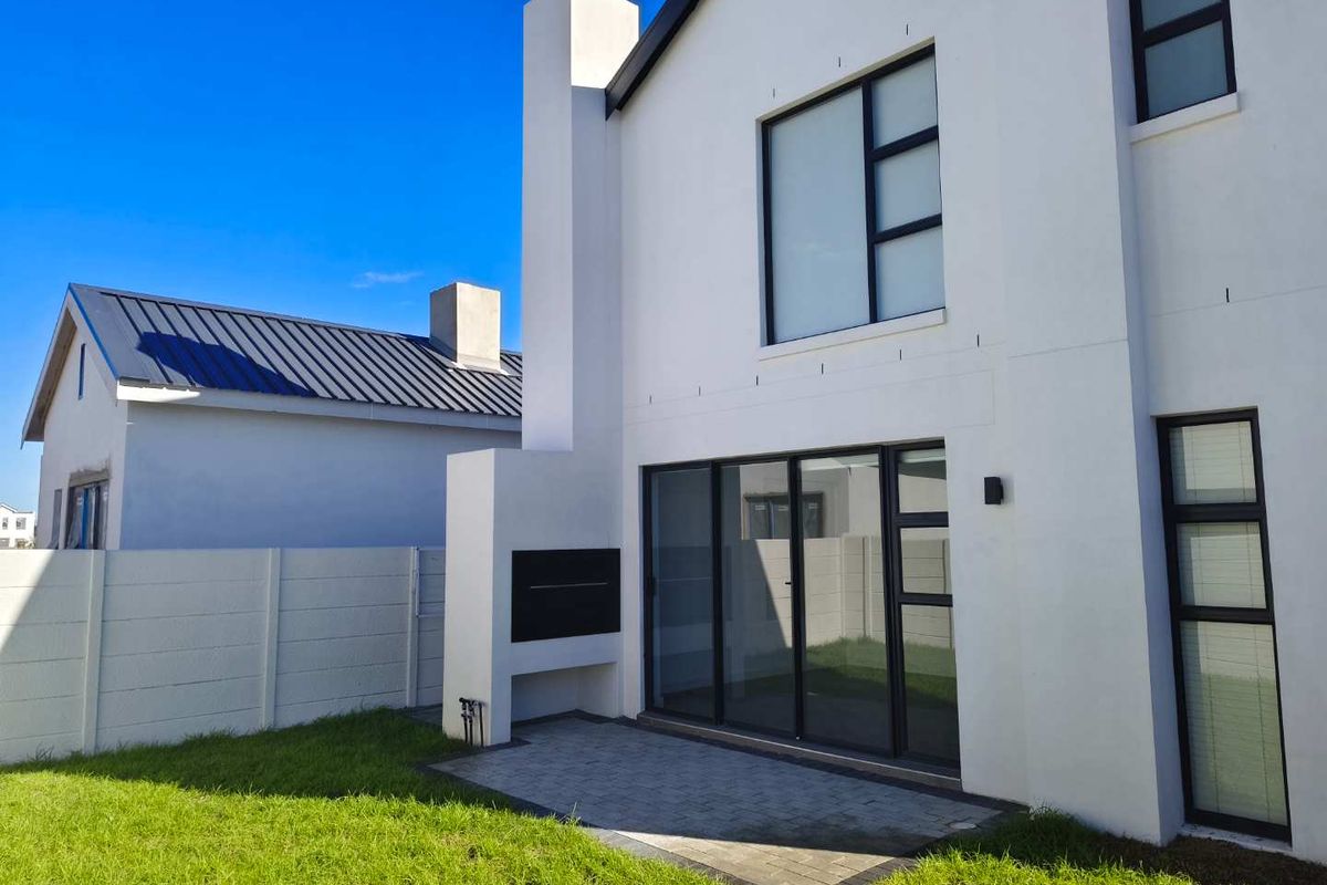 Rear view of a modern two-story home featuring a paved patio, built-in outdoor fireplace, and large sliding glass doors leading to the garden.