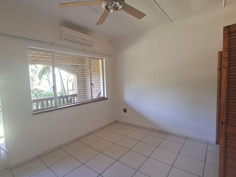A bright, empty bedroom featuring tiled flooring, a ceiling fan, a split-system air conditioner, and a built-in cupboard.