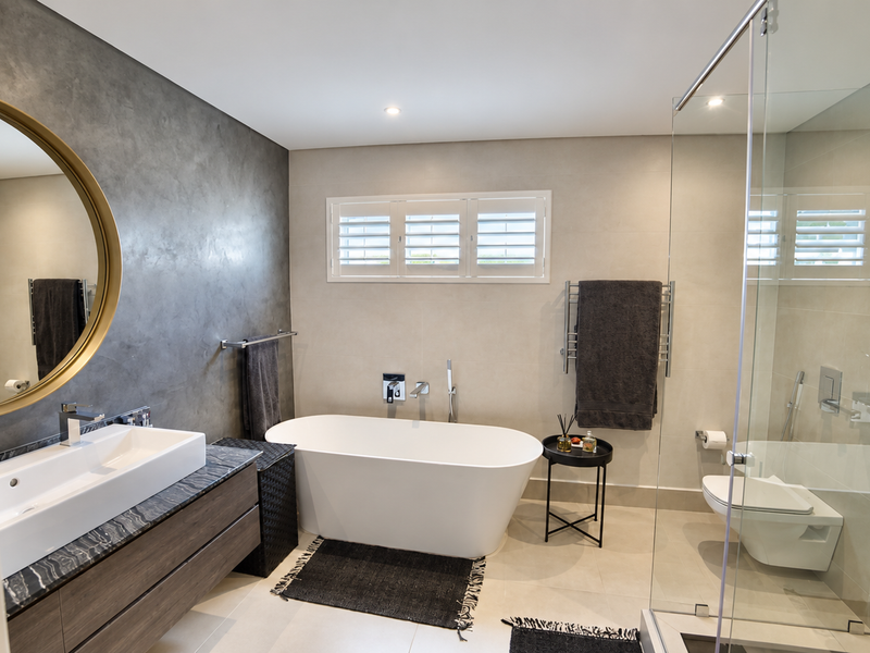 Modern bathroom featuring a sleek floating vanity, freestanding bathtub, glass-enclosed shower, wall-mounted toilet, and elegant plantation shutters.