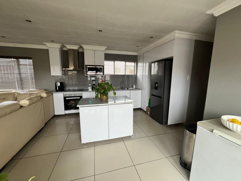Modern open-plan kitchen featuring sleek white cabinetry, a central island, built-in appliances, and large format floor tiles, seamlessly integrated with the living area.