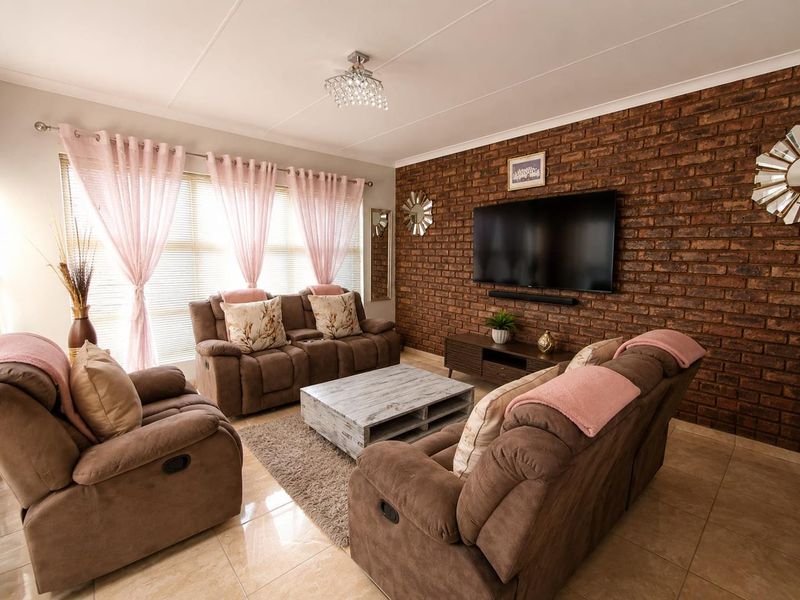 A well-maintained living room featuring a prominent exposed brick feature wall, polished tile flooring, and elegant crystal lighting.